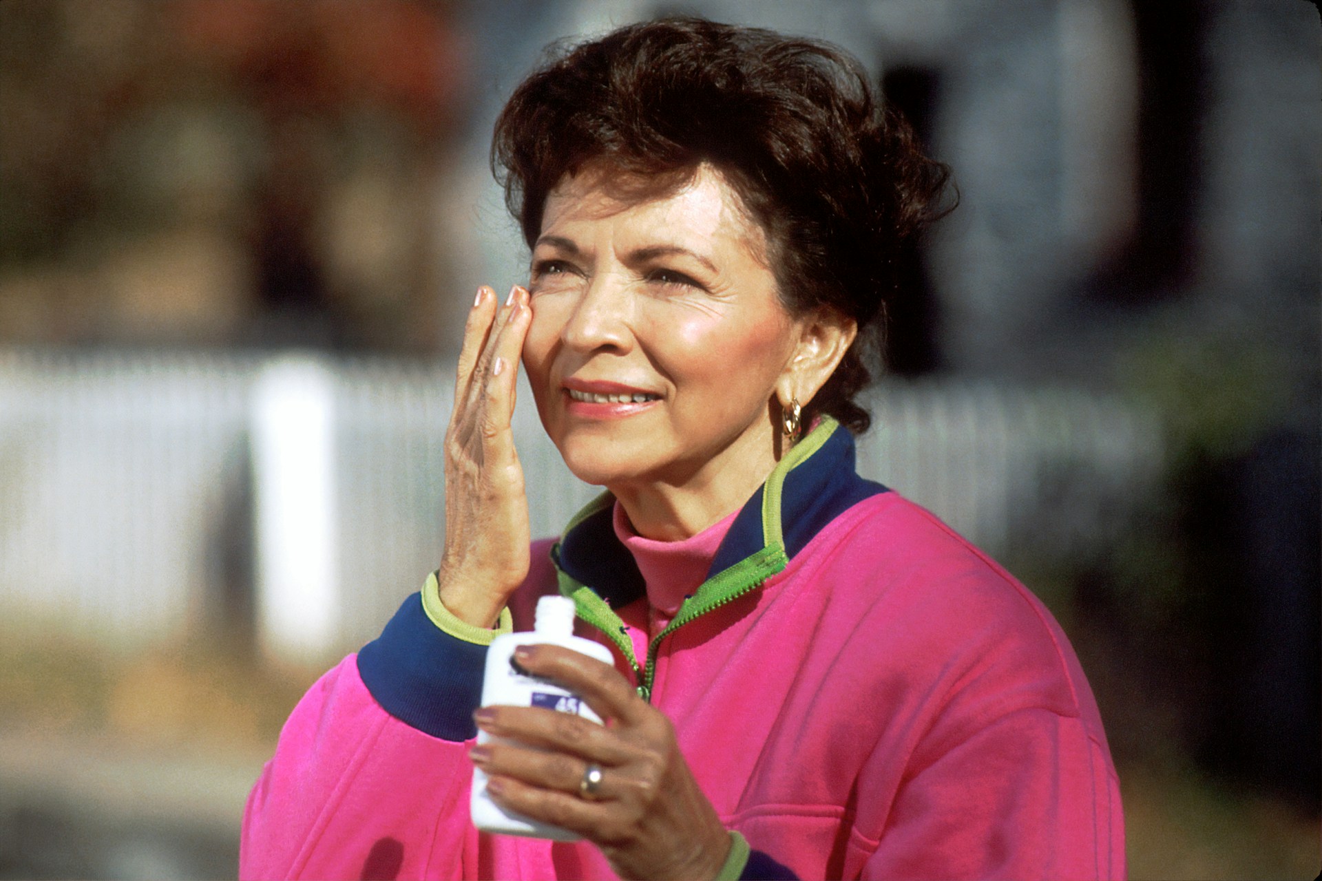 An older woman putting sunscreen on her face